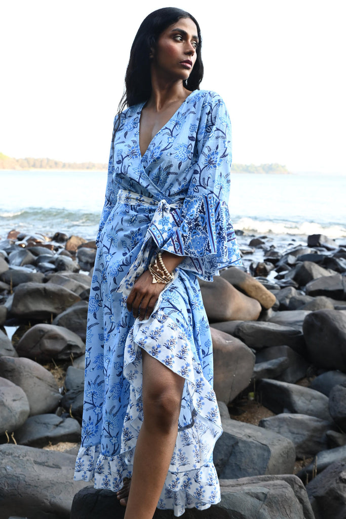 Person wearing a blue floral dress standing against a stone wall.