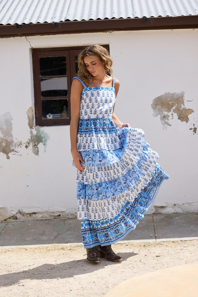 Woman wearing a blue and white patterned dress standing in front of a white wall.