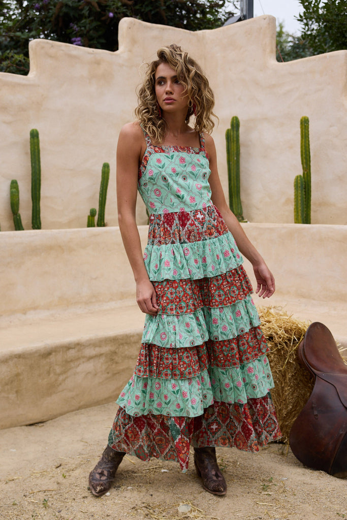 Woman in a floral dress standing in a desert-like setting with cacti and a saddle.