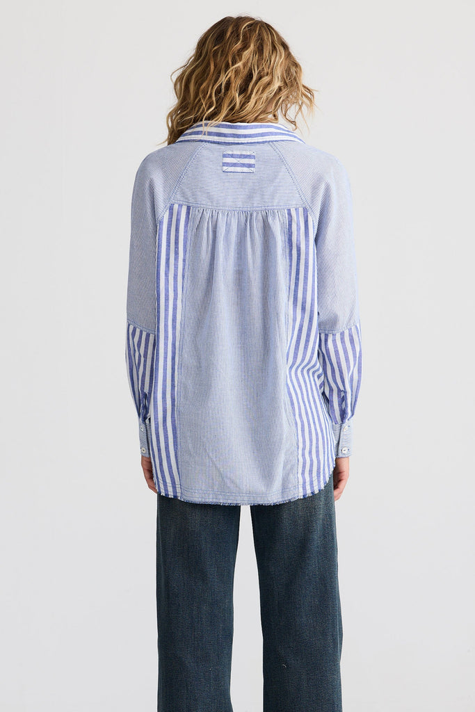 Person wearing a light blue striped shirt and dark jeans on a white background