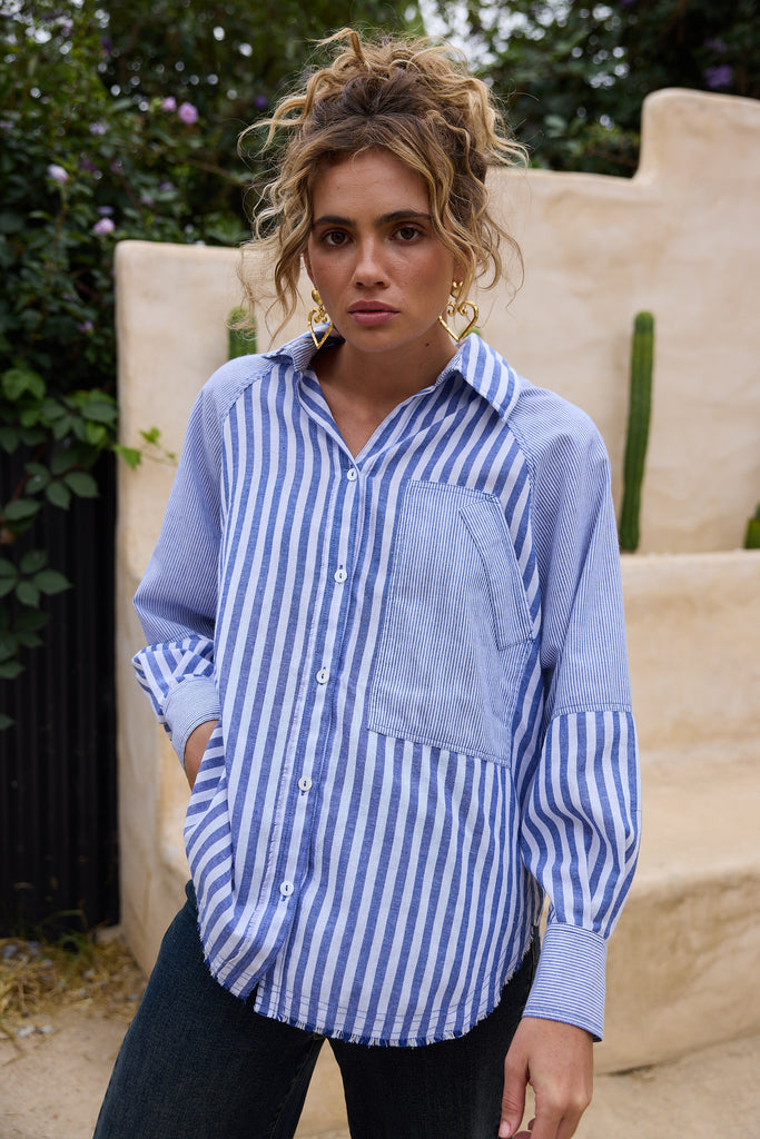 Woman wearing a blue and white striped shirt with a pocket, standing outdoors.