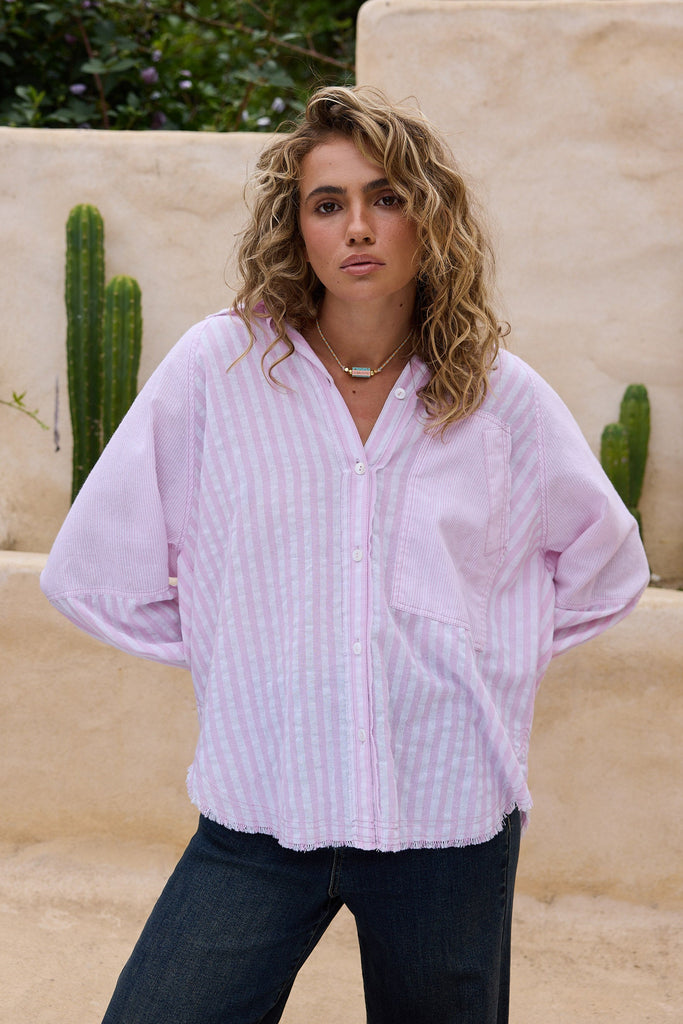 Woman wearing a light pink shirt and dark pants standing in front of a beige wall with cacti.
