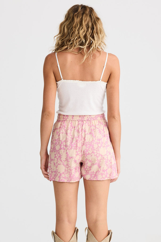 Woman wearing a white top and pink floral shorts with beige boots on a white background