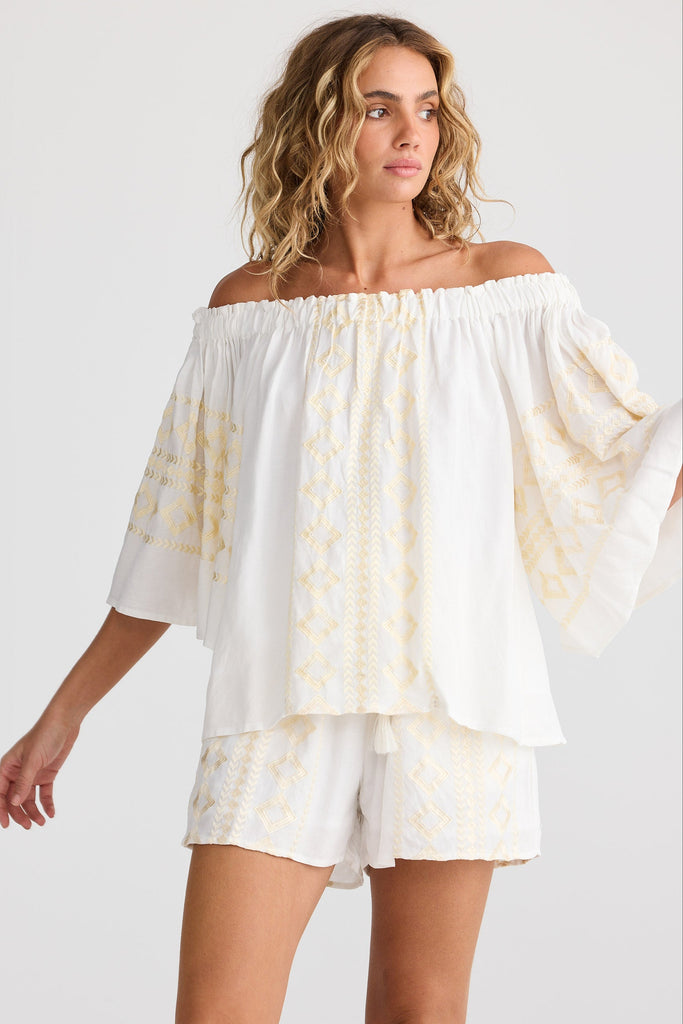 Woman wearing a white off-shoulder top and shorts on a plain background