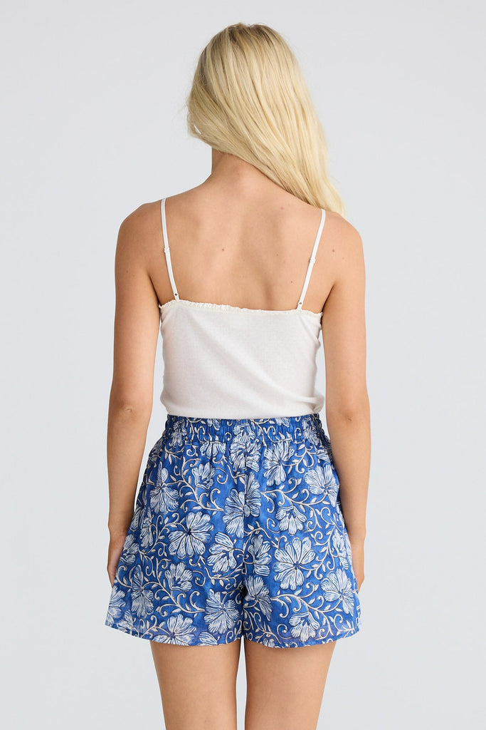 Woman wearing a white top and blue floral shorts on a white background