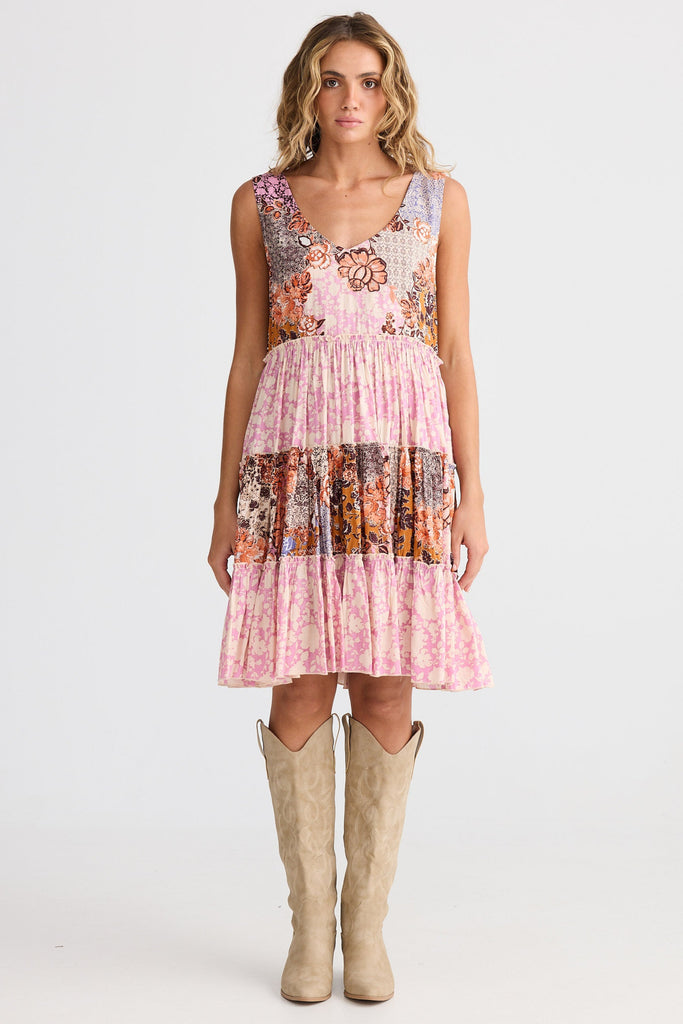 Woman wearing a floral dress with pink accents and beige boots on a white background
