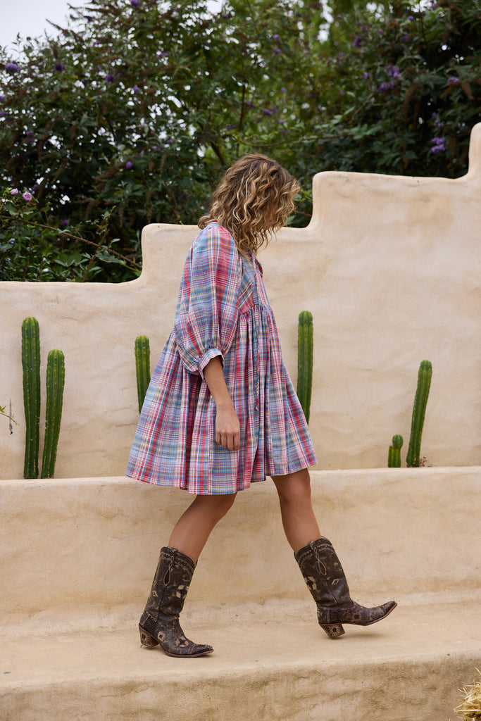 Woman in a plaid dress and boots walking on steps with cacti and a wall in the background
