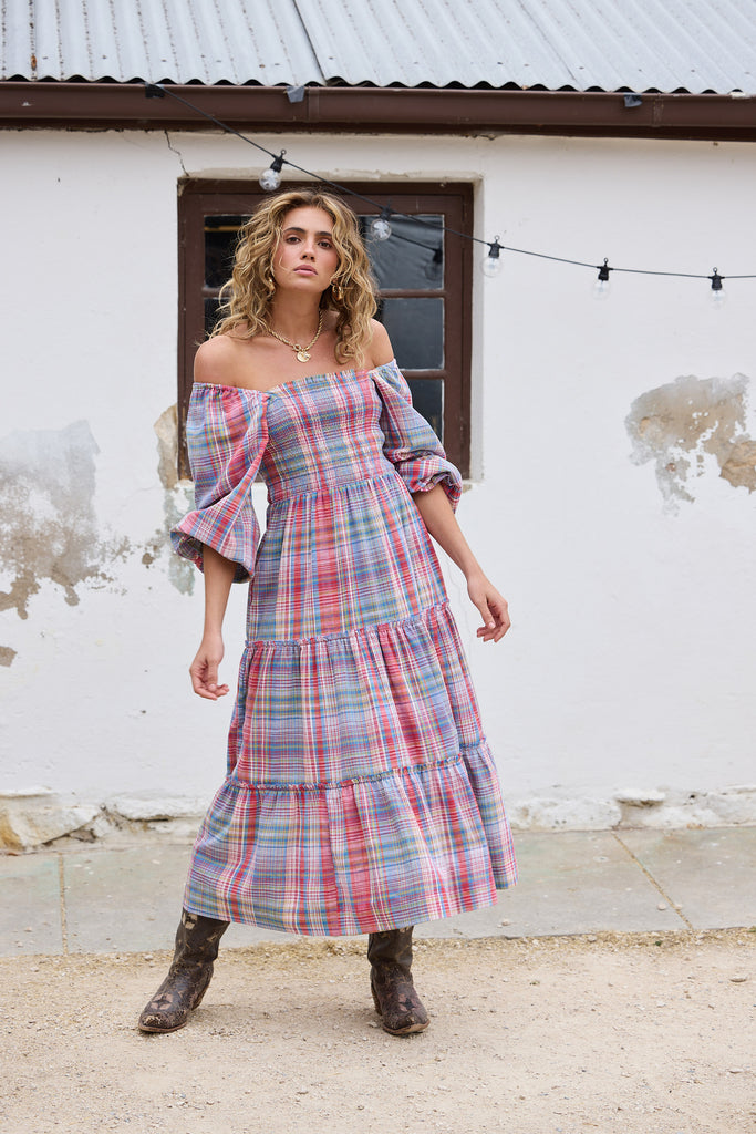 Woman wearing a plaid dress standing in front of a rustic building.