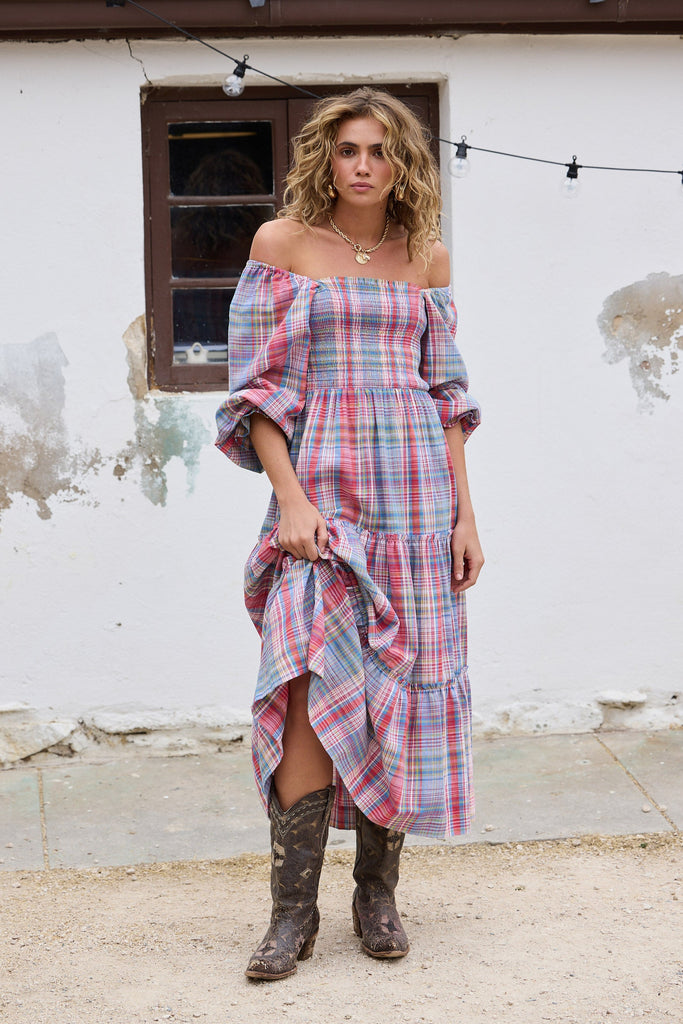 Woman wearing a plaid dress and boots standing in front of a rustic building.