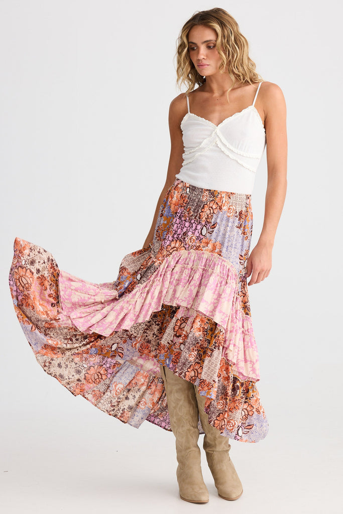 Woman wearing a long, patterned skirt with a white top on a white background