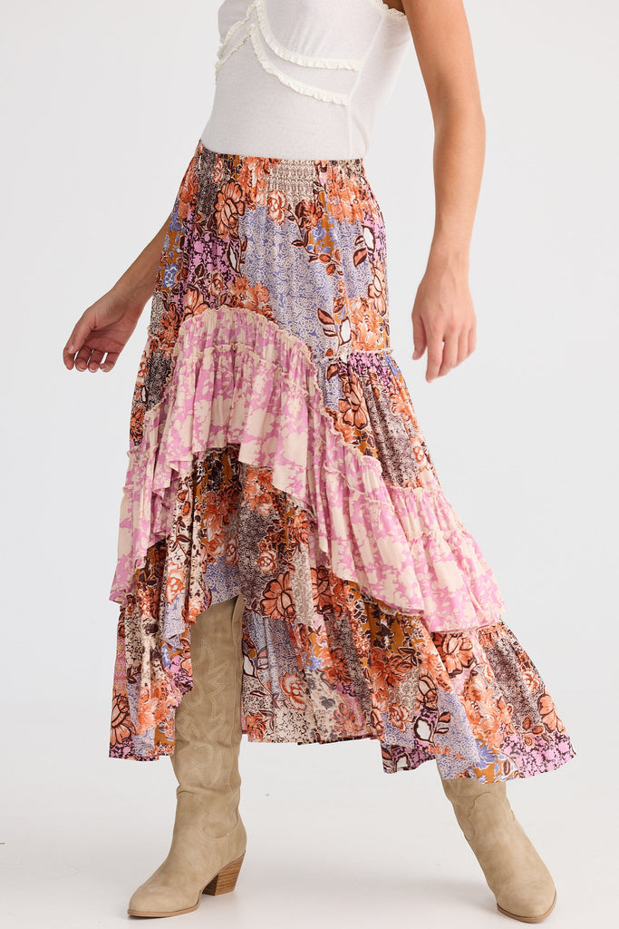 Woman wearing a colorful tiered skirt with a white top and beige boots on a white background