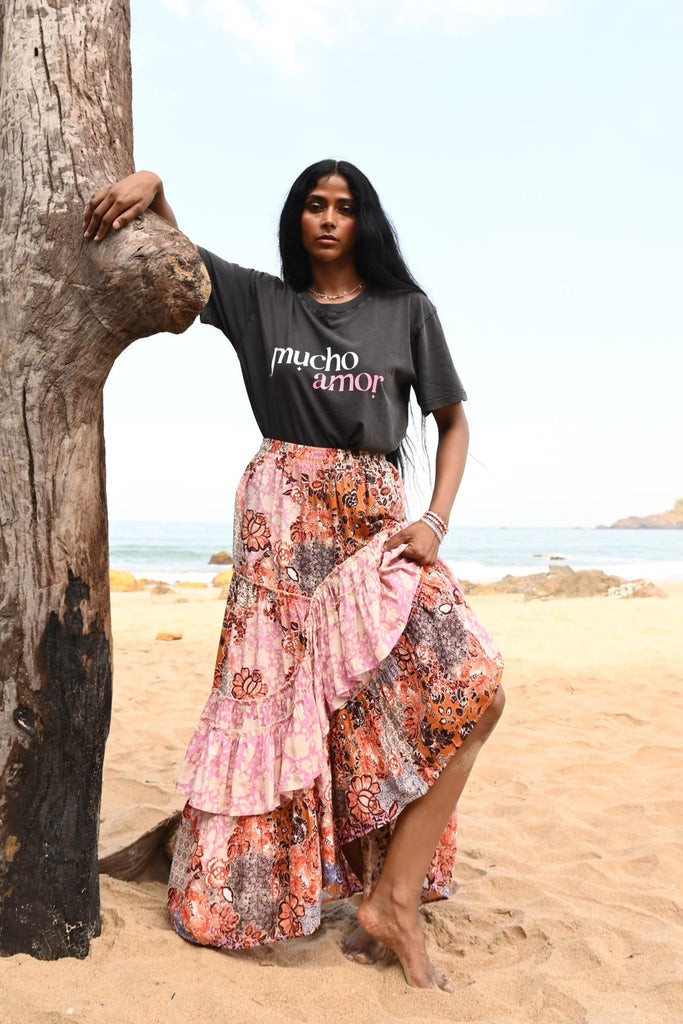 Woman leaning on a log wearing a dark grey t-shirt and a floral skirt.