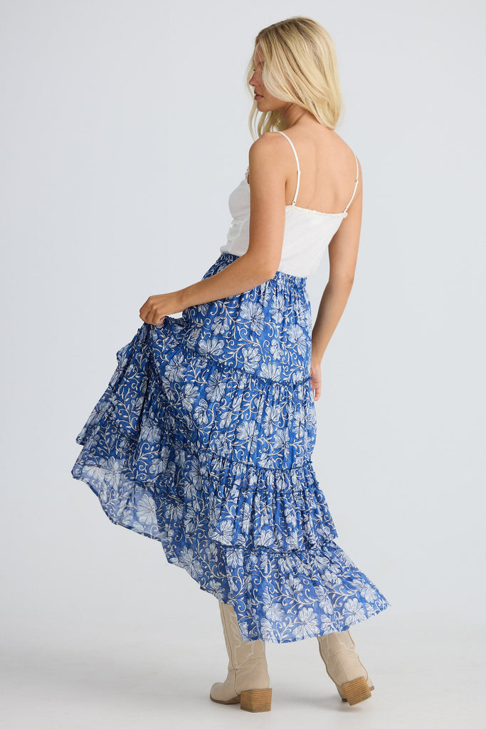 Woman wearing a blue floral skirt and white top on a plain background