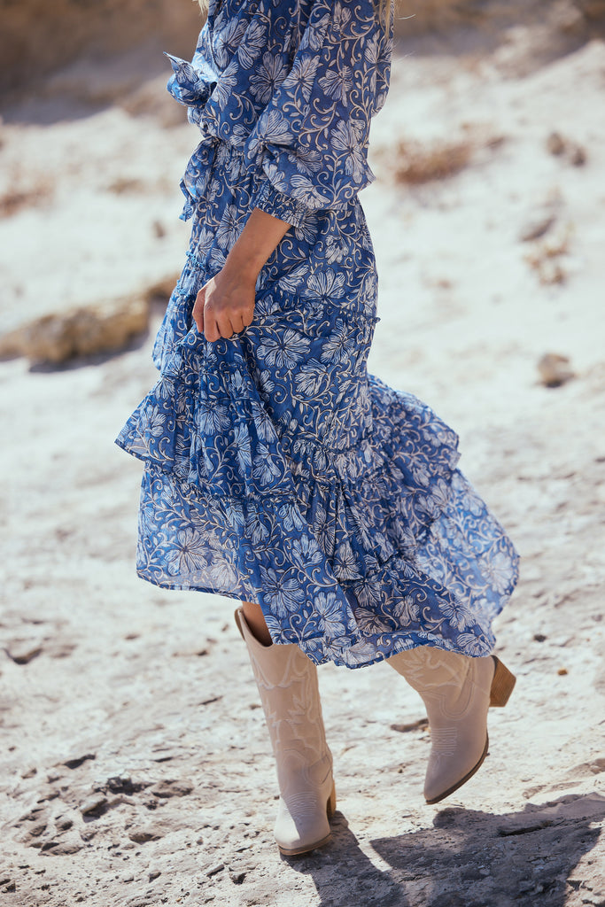Person wearing a blue floral skirt and shirt and beige boots on a rocky surface