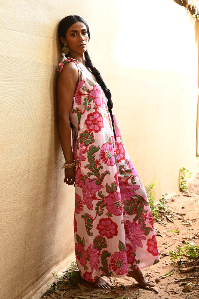 Woman wearing a floral jumpsuit standing against a light-colored wall.