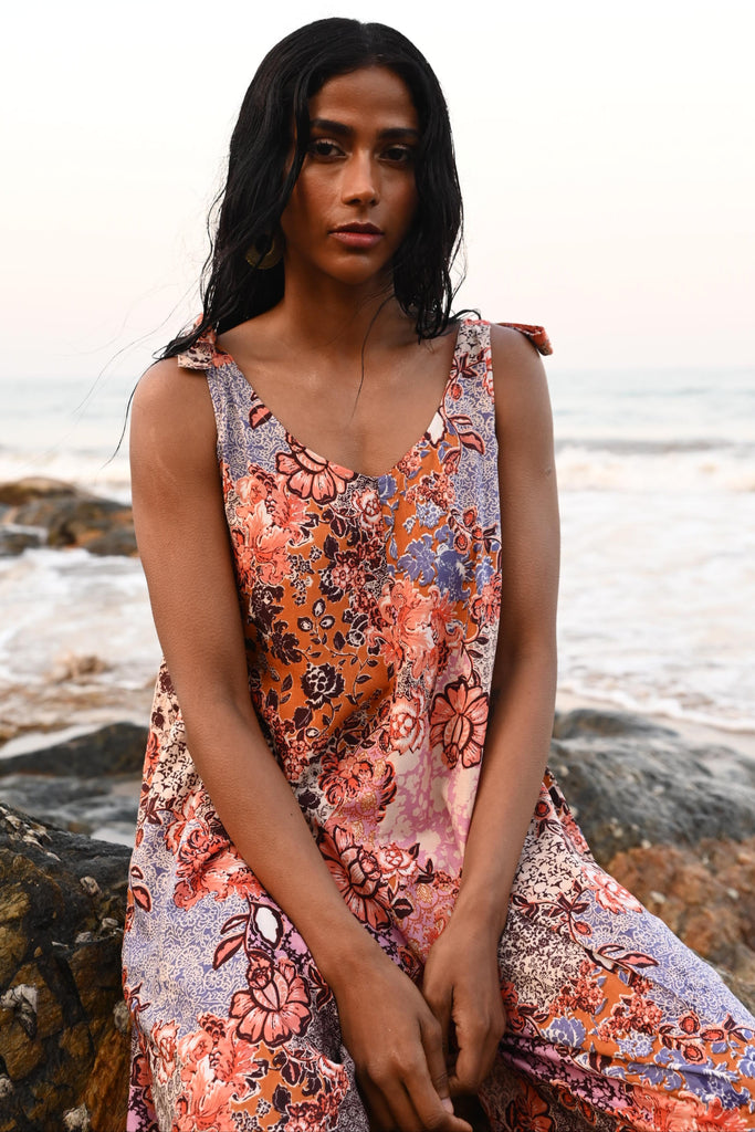 Woman in a floral jumpsuit sitting on a rock by the beach