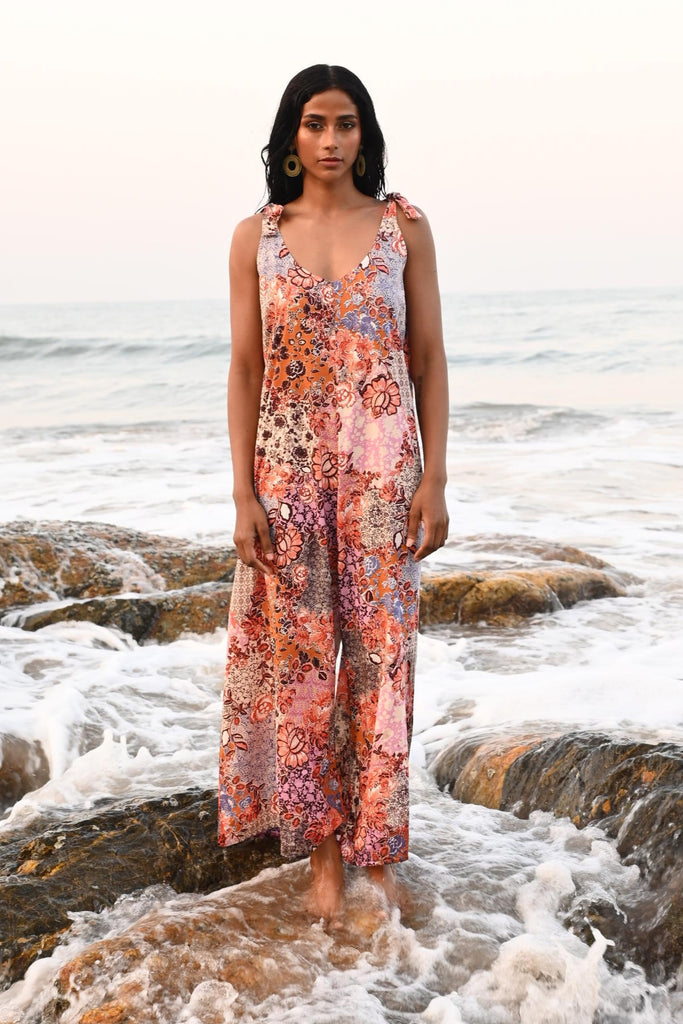 Woman in a floral jumpsuit standing on a rocky beach surrounded by waves