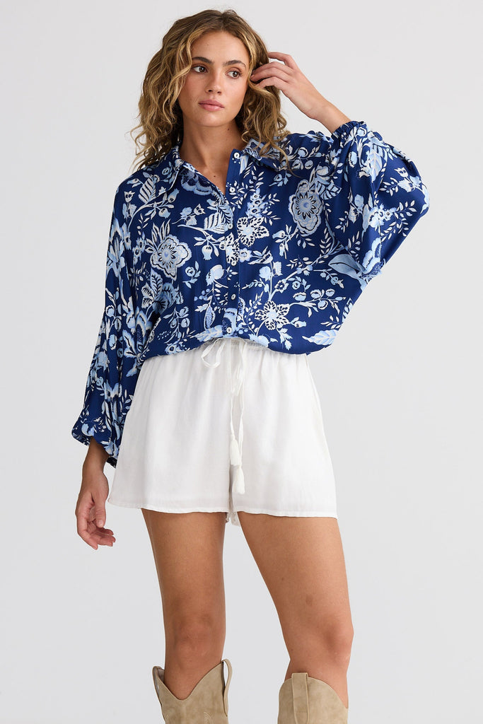 Woman wearing a blue floral blouse, white shorts, and beige knee-high boots on a white background