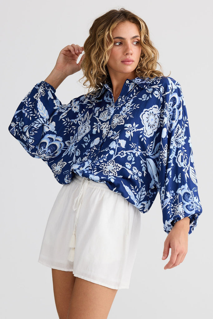 Woman wearing a blue floral blouse and white shorts on a plain background