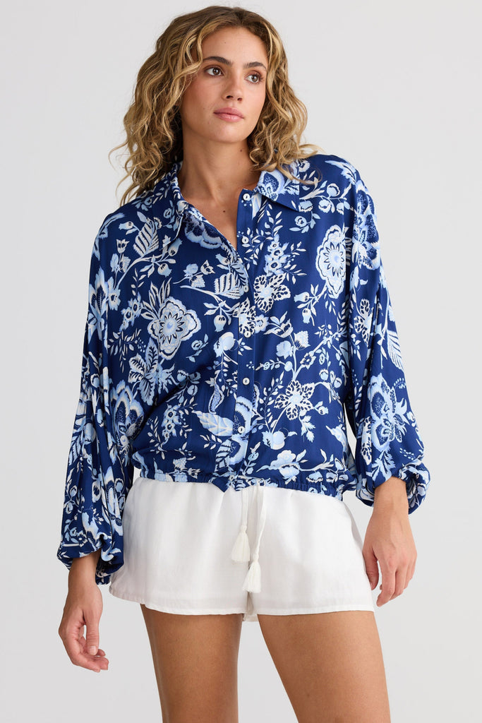 Woman wearing a blue floral blouse and white shorts on a plain background