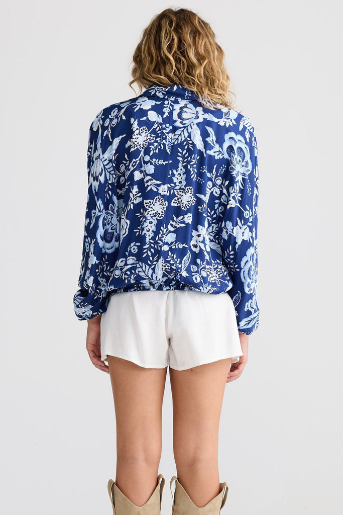Person wearing a blue floral blouse, white shorts, and tan cowboy boots on a plain background