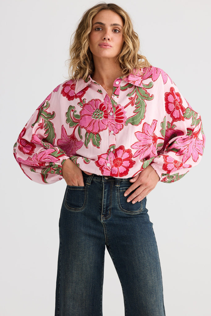 Woman wearing a pink floral blouse and blue jeans on a white background