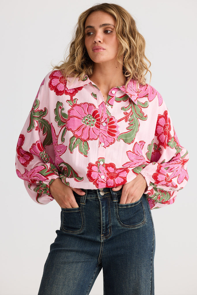 Woman wearing a pink floral blouse and blue jeans on a white background