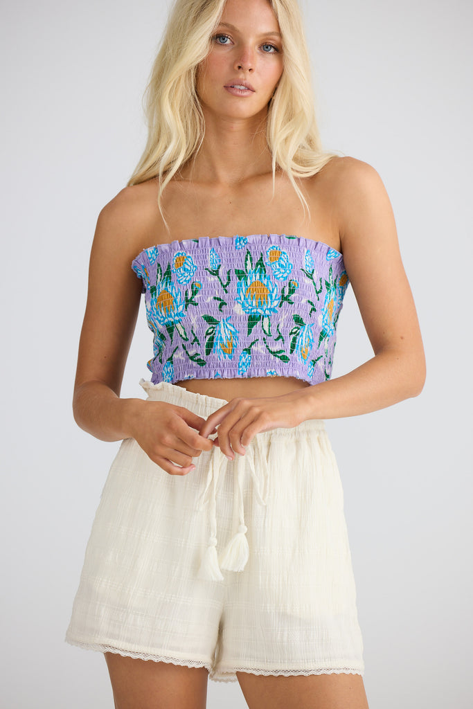 Woman wearing a floral strapless top and white shorts on a plain background
