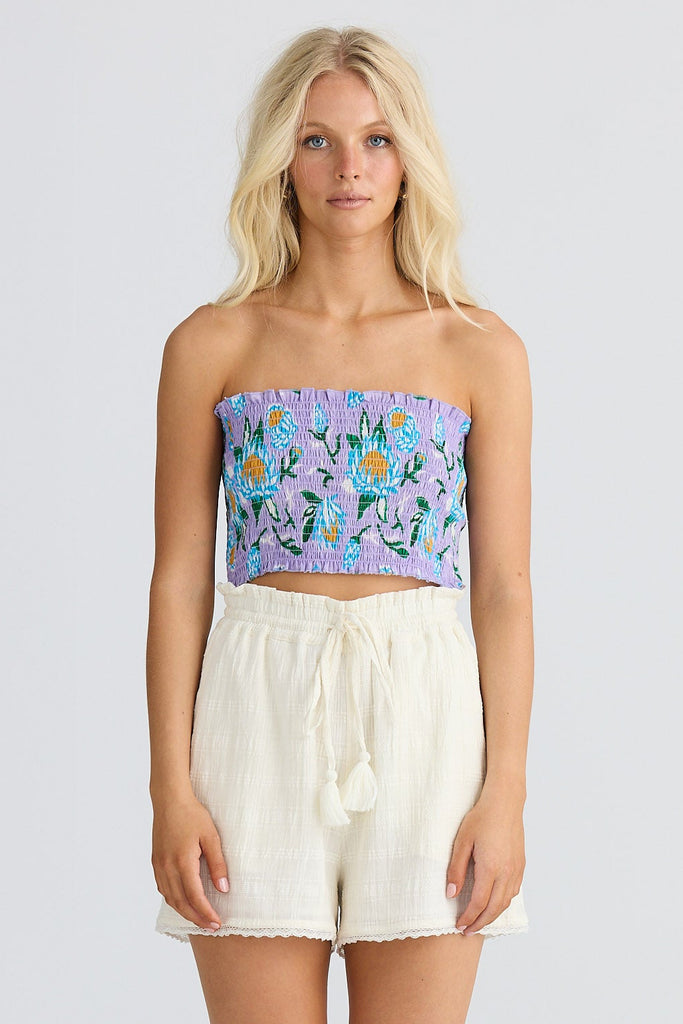 Woman wearing a floral strapless top and white shorts on a white background
