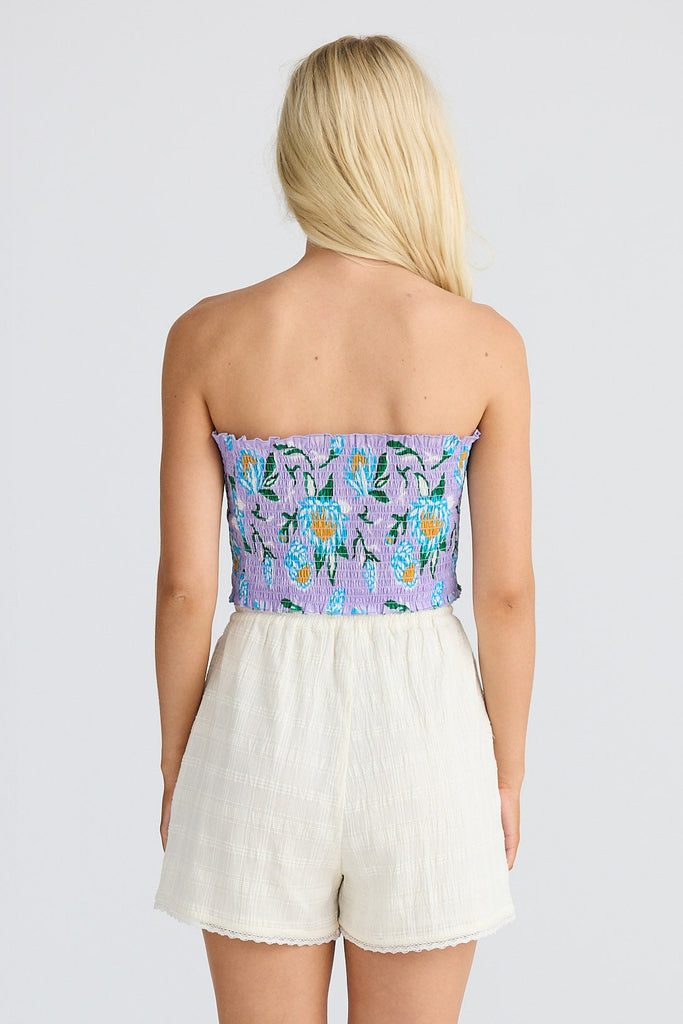 Woman wearing a strapless floral top and white shorts on a plain background