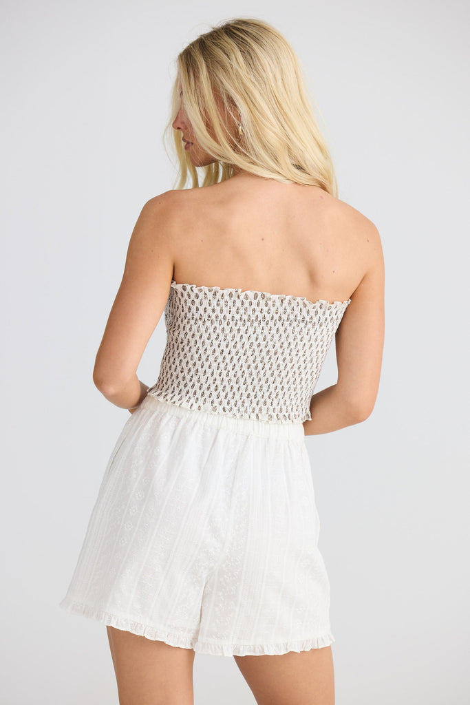 Woman wearing a strapless patterned top and white shorts on a plain background