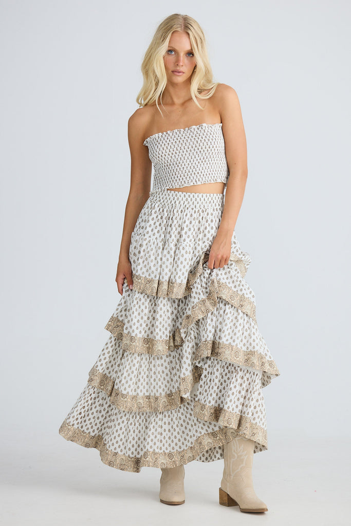 Woman wearing a white strapless top and ruffled skirt with beige accents on a light gray background