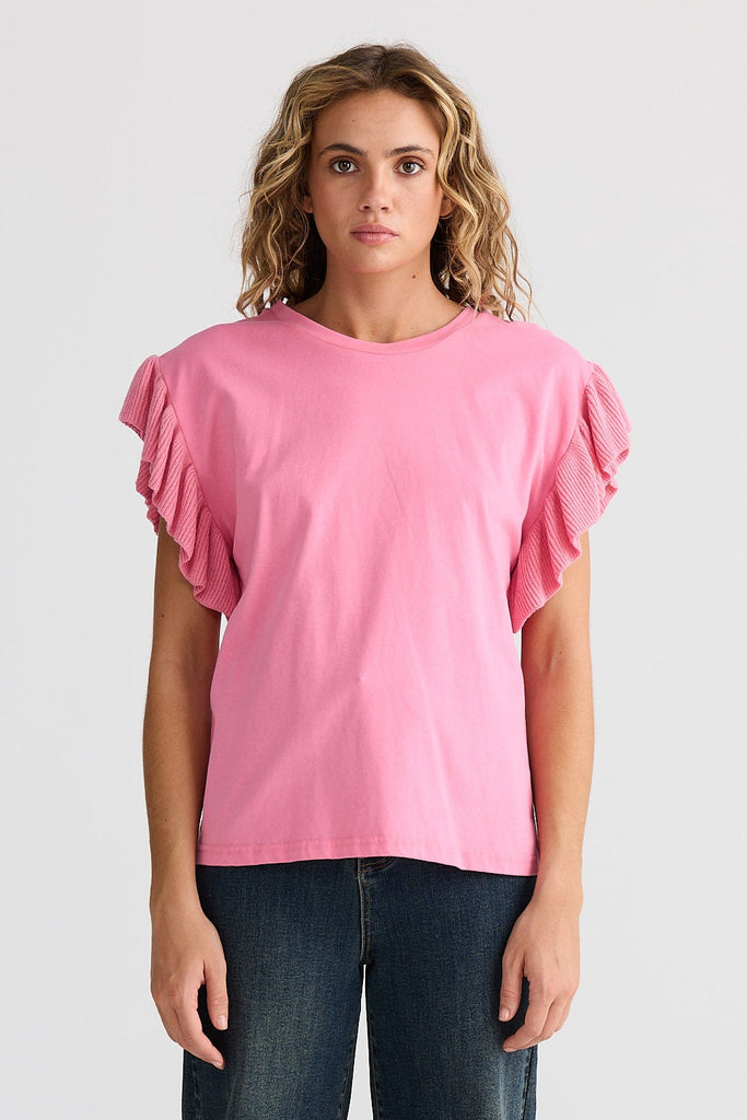 Woman wearing a pink blouse with ruffled sleeves and dark jeans on a white background