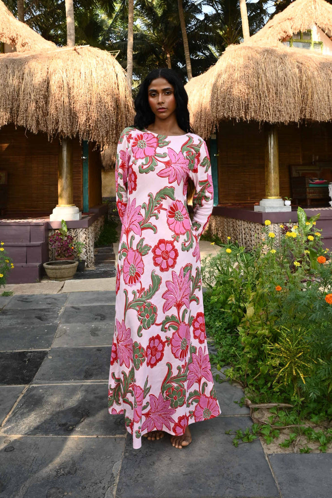 Woman in a floral dress standing in a tropical setting with palm trees and a thatched-roof hut.