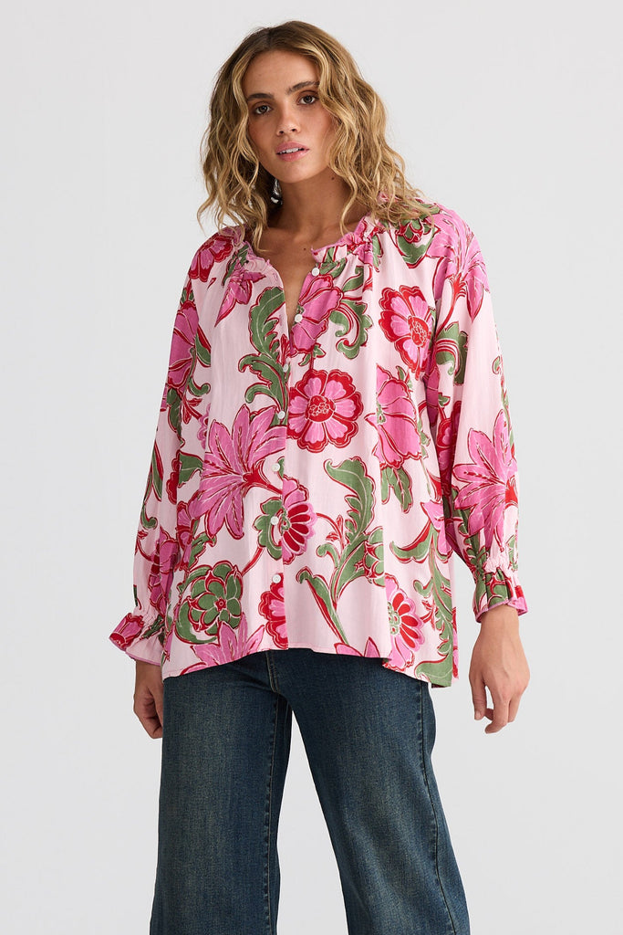 Woman wearing a pink floral blouse and blue jeans on a white background