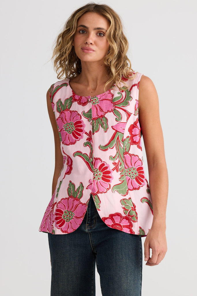 Woman wearing a sleeveless floral top with pink flowers and green leaves on a plain background