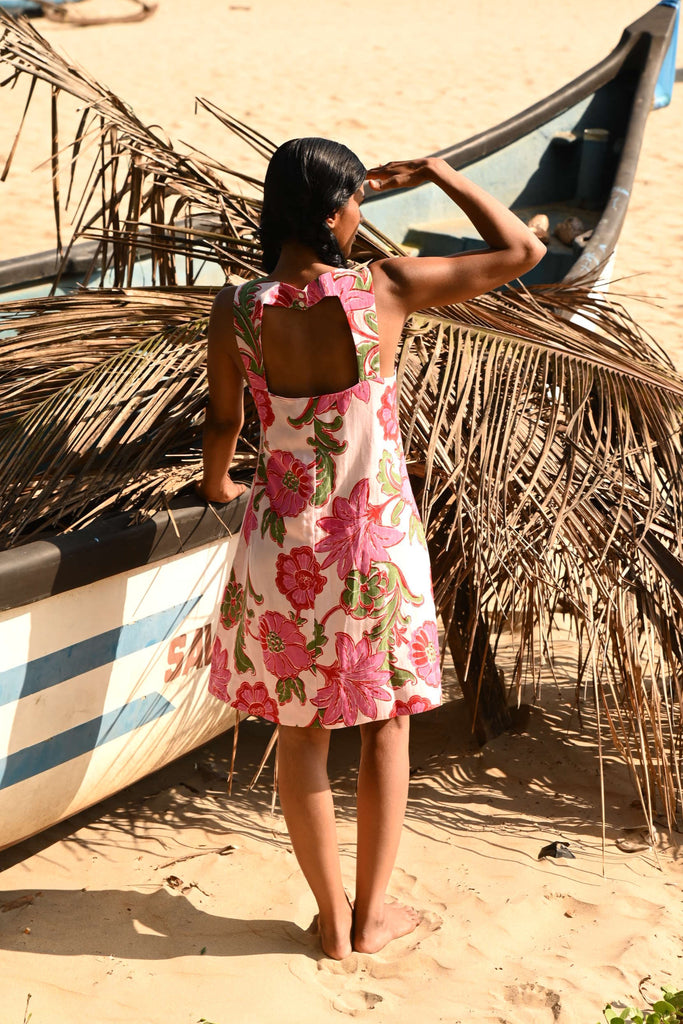Woman in a floral dress standing next to a traditional fishing boat on a beach.