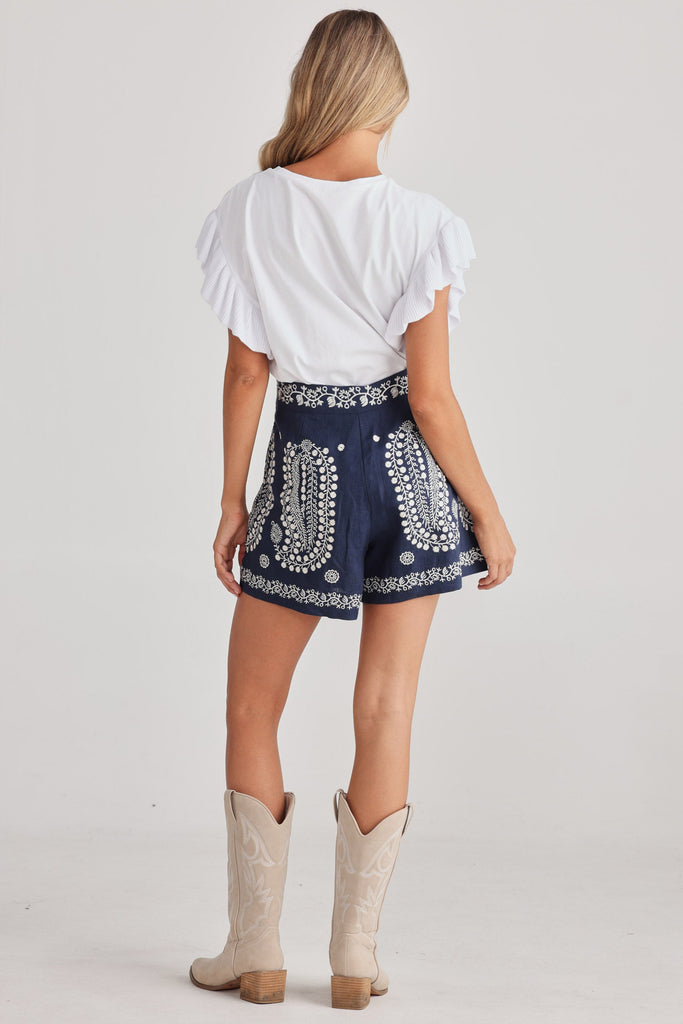 Person wearing a white top and navy shorts with white patterns, standing against a plain background.