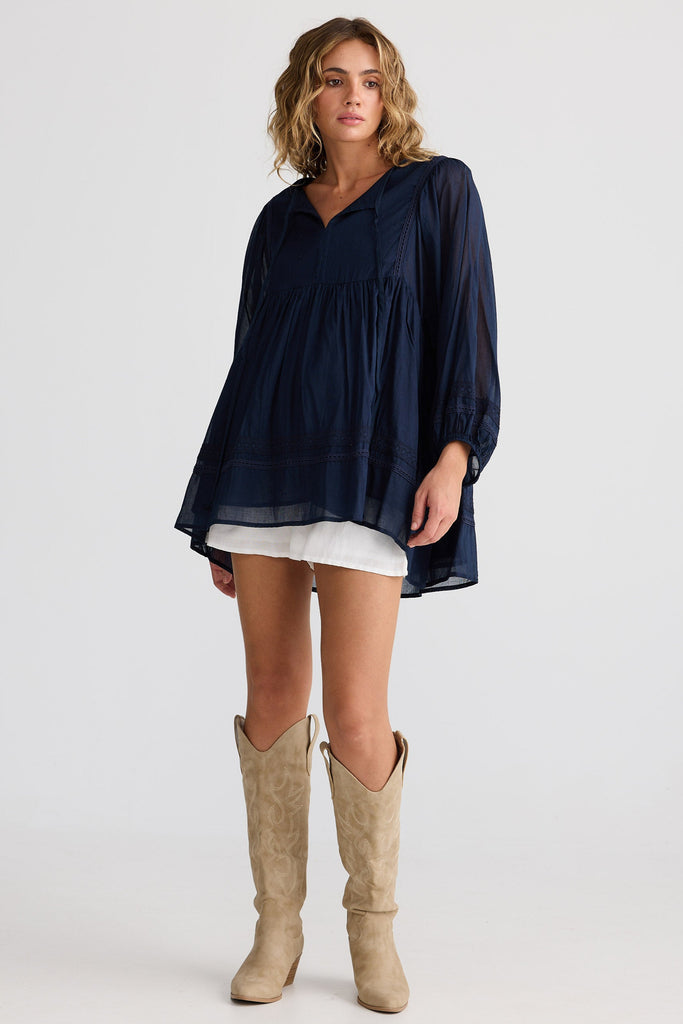 Woman wearing a navy blue oversized shirt and beige knee-high boots on a white background