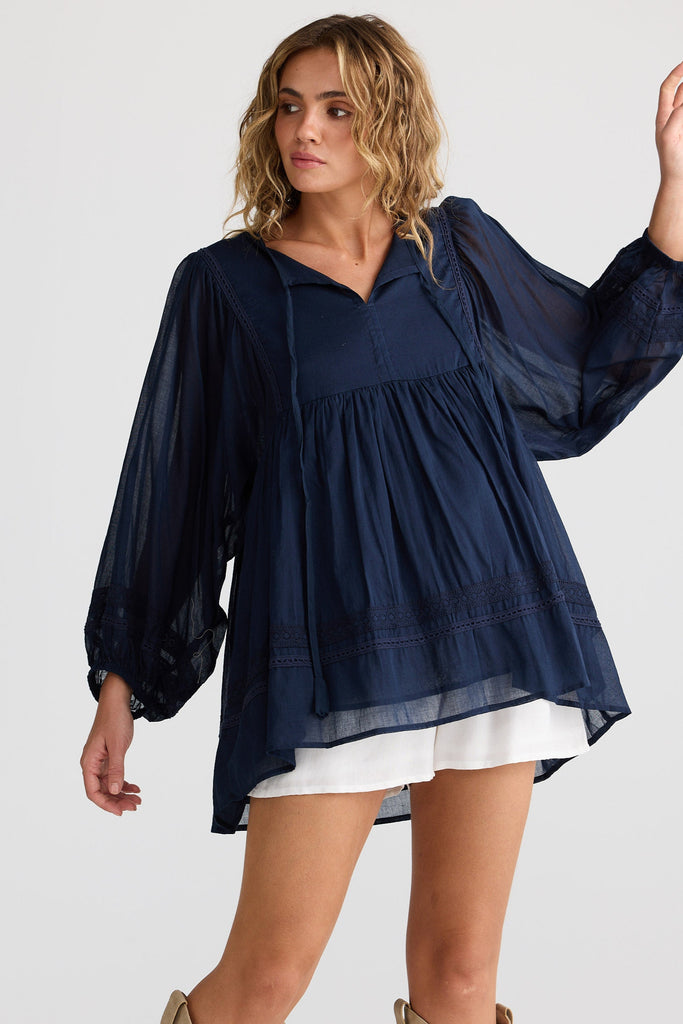 Woman wearing a navy blue blouse with white shorts on a plain background