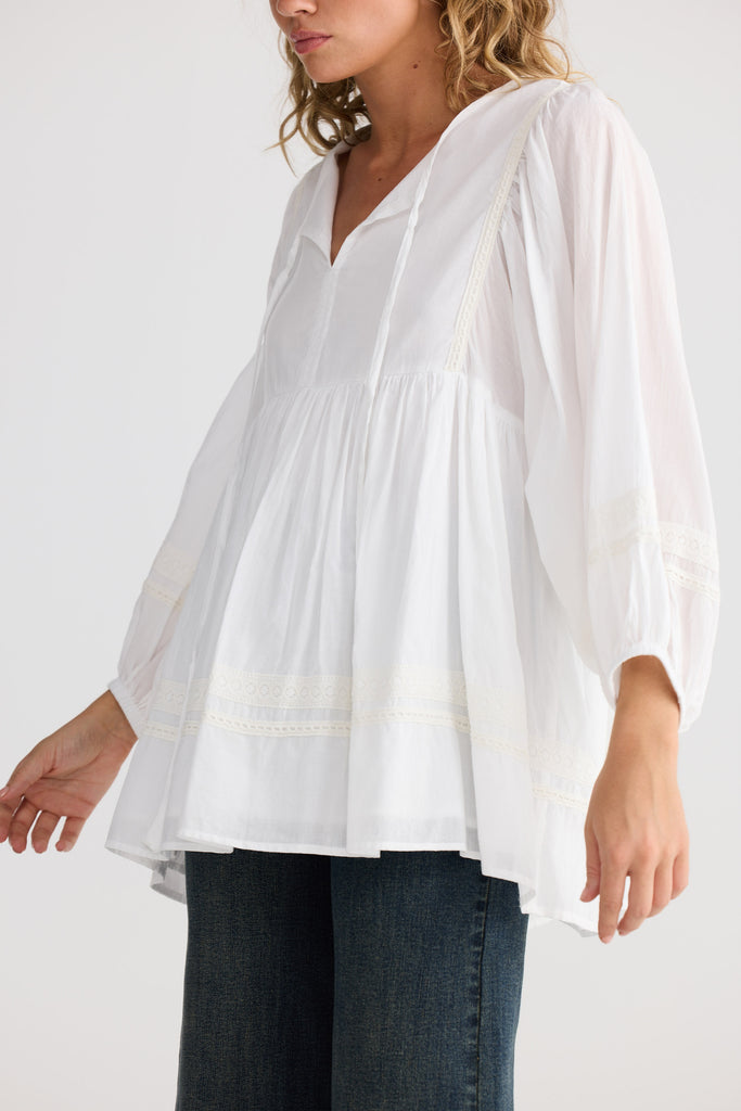 Woman wearing a white blouse and dark jeans on a plain background