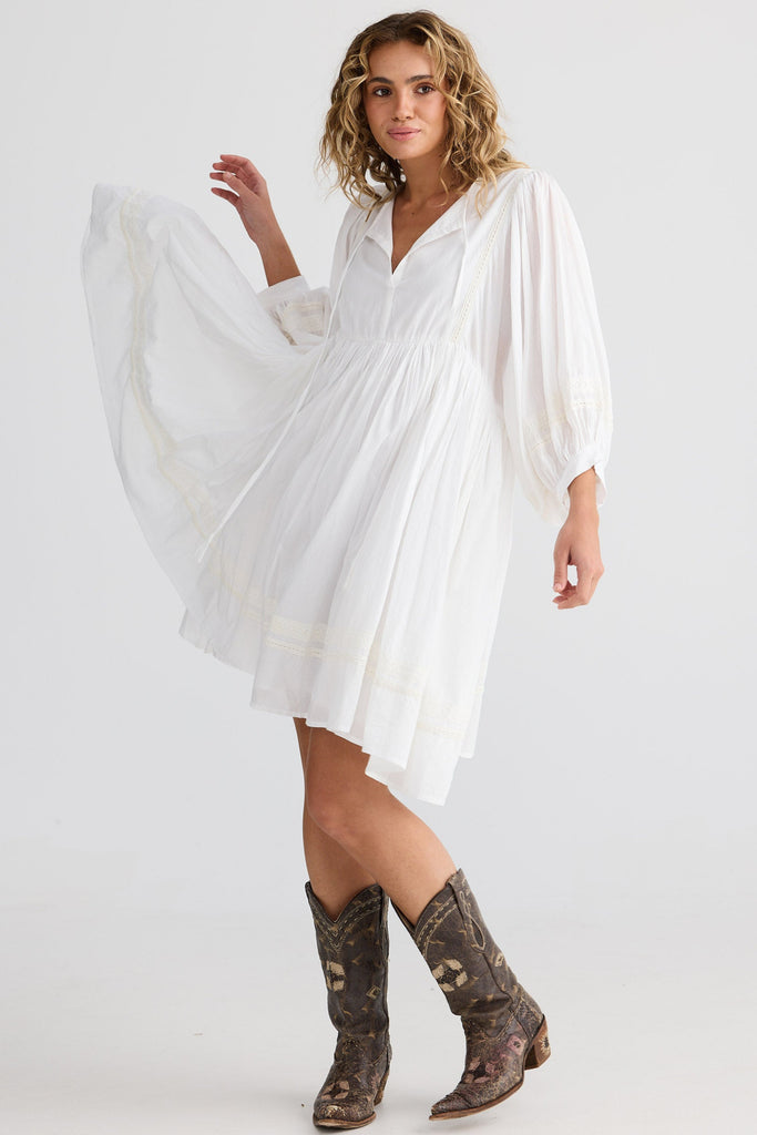 Woman wearing a white dress with long sleeves and brown boots on a white background