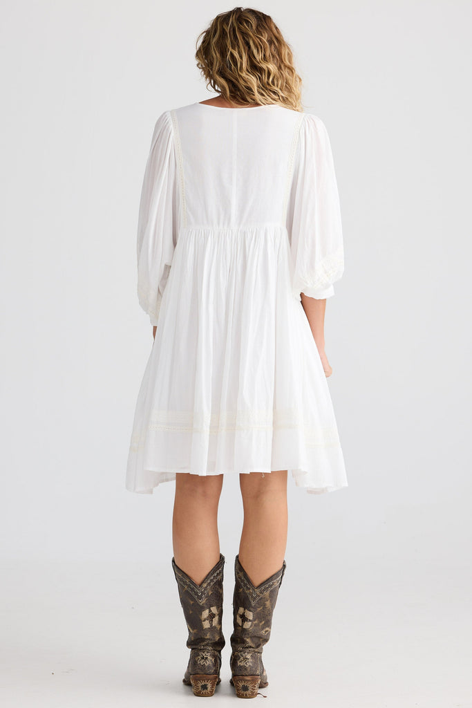 Person wearing a white dress and cowboy boots on a plain background