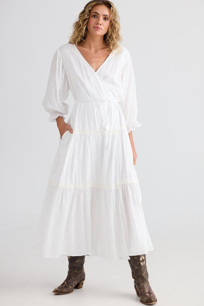 Woman wearing a white dress with long sleeves and brown boots on a white background