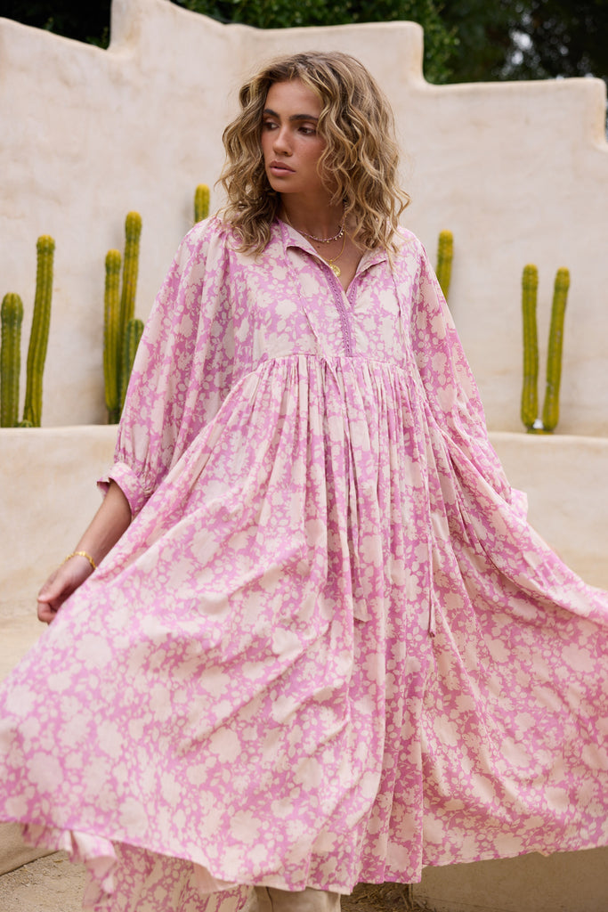 Woman wearing a pink floral dress sitting outdoors with cacti in the background