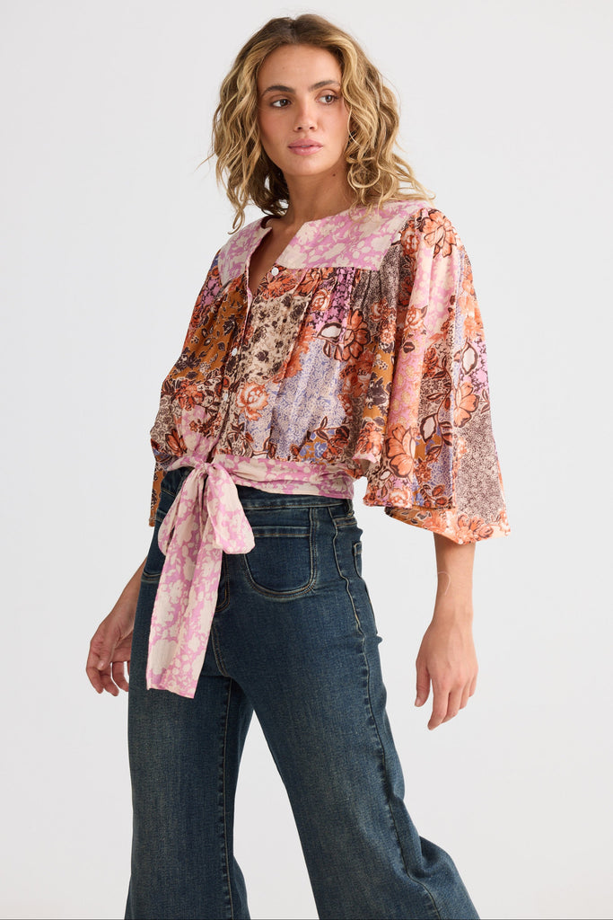 Woman wearing a patterned blouse and jeans on a white background