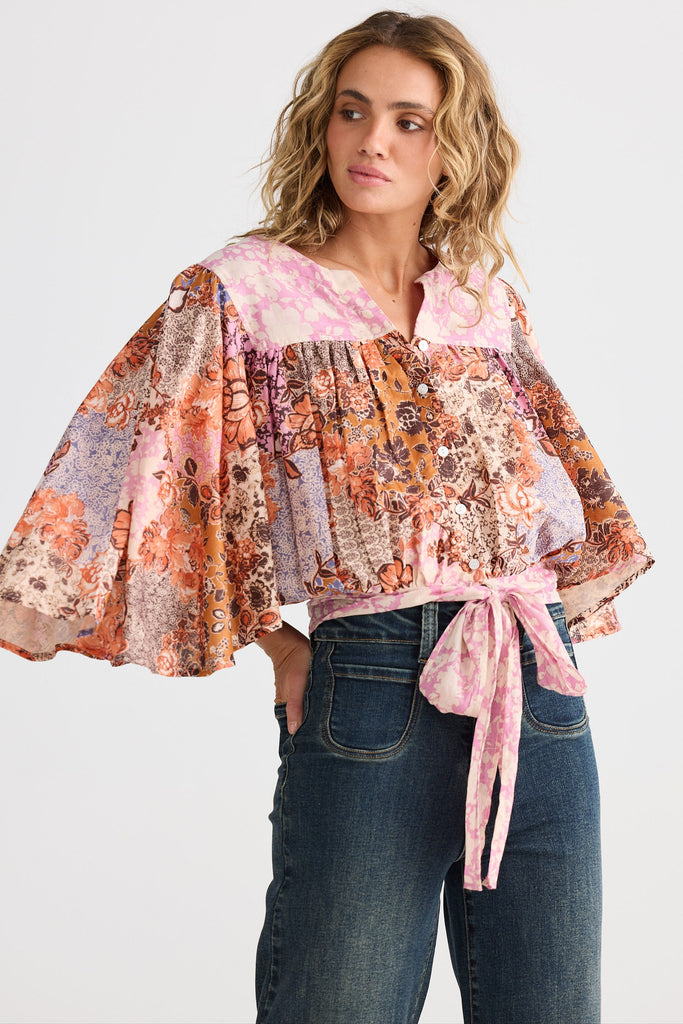 Woman wearing a floral blouse with a tie waist and jeans on a white background