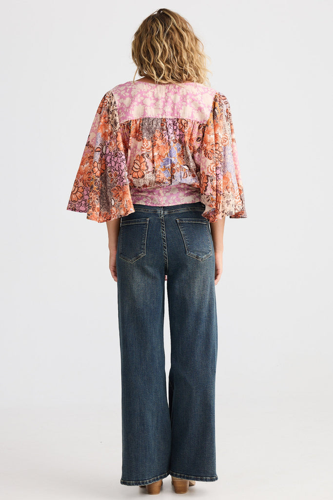 Person wearing a patterned blouse and blue jeans on a white background