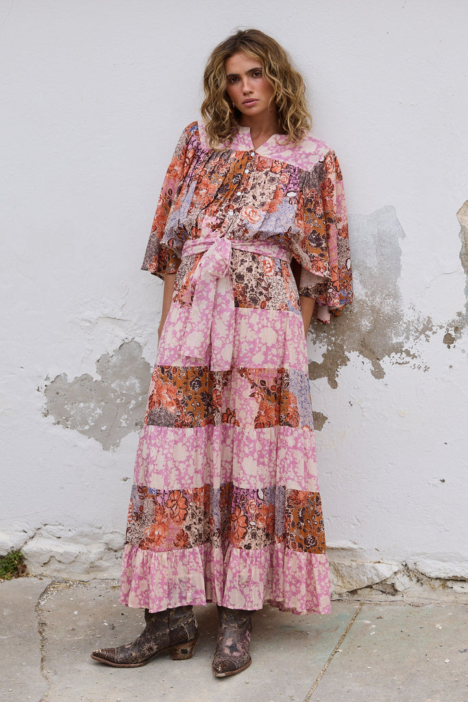 Woman wearing a floral dress standing against a white wall.