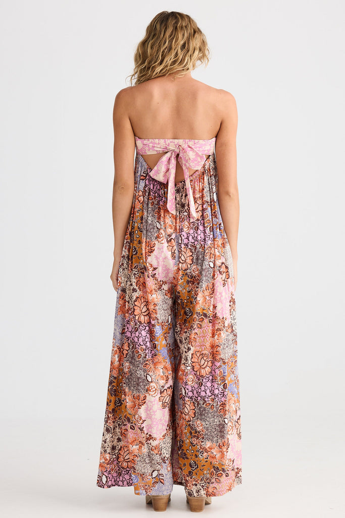 Woman wearing a strapless floral jumpsuit with a bow detail on a white background